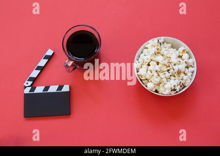 Bowl of popcorn and film clapper isolated on red background. Top view. Fatty and unhealthy snacks. Movie time. Entertainment industry. Minimalist back Stock Photo