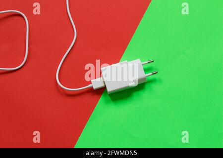 White phone charger isolated on half red half green background. Technological devices. Stock Photo