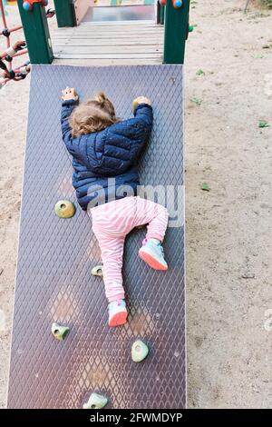 Toddler Girl Climbing A Wall In A Park Stock Photo