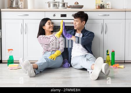 Tired asian couple sitting in kitchen, giving high five Stock Photo