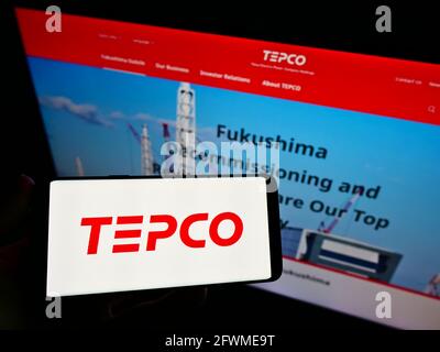 Person holding smartphone with logo of Tokyo Electric Power Company Holdings Inc. (TEPCO) on screen in front of web page. Focus on cellphone display. Stock Photo
