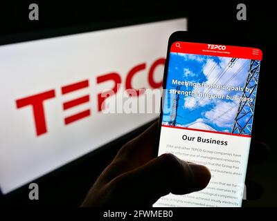 Person holding cellphone with webpage of Tokyo Electric Power Company Holdings Inc. (TEPCO) on screen with logo. Focus on center of phone display. Stock Photo