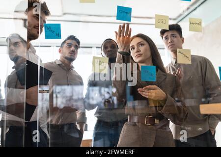 Colleagues having meeting using sticky notes on glass wall Stock Photo
