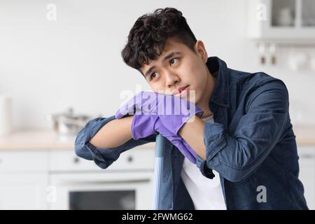 Tired asian guy leaning on broom, looking at copy space Stock Photo