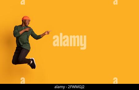Cheerful black hipster guy jumping up in air and pointing aside Stock Photo