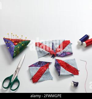 Pieces of fabric laid out in the shape of a patchwork block, sewing and quilting accessories. Space for text. Stock Photo