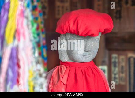 tokyo, japan - may 20 2021: Close up on the face of a Jizo statue symbol of filial piety to protect children and wearing a red knit cap with a baby bi Stock Photo