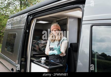 woman putting rubber gloves on in her camper van washing up happily Stock Photo