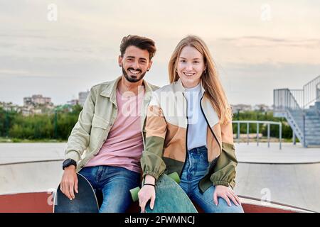 Young multiracial couple looks at the camera smiling in a skate park Stock Photo