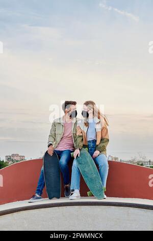 Young couple in masks look at each other in a skate park Stock Photo