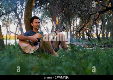 young man playing guitar sitting on a tree Stock Photo