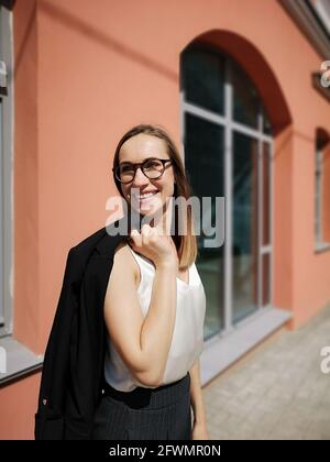 Young businesswoman yanks in hand jacket and smiles broadly Stock Photo