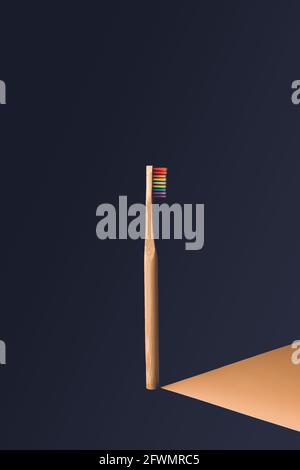 vertical rainbow wooden toothbrush in center of image with dark blue background with orange shadow effect projected to the right Stock Photo