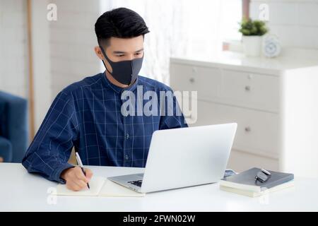 Young asian business man in face mask for protect covid-19 and work on laptop computer and writing notebook, businessman quarantine work from home, ne Stock Photo