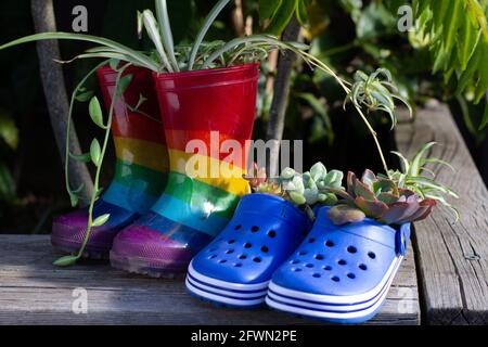 Recycled childrens boots and shoes in garden used as plant pots, a fun way to encourage recycle reuse and reduce waste. Stock Photo