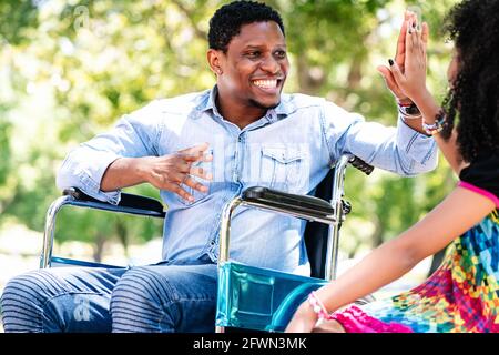 Man in a wheelchair at the park with his daughter. Stock Photo