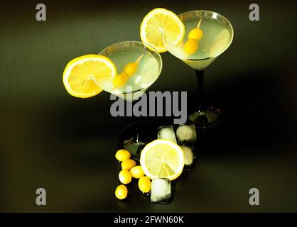 Two glasses of martini with lemon, olives on a black background, next to ice cubes. Close-up. Stock Photo