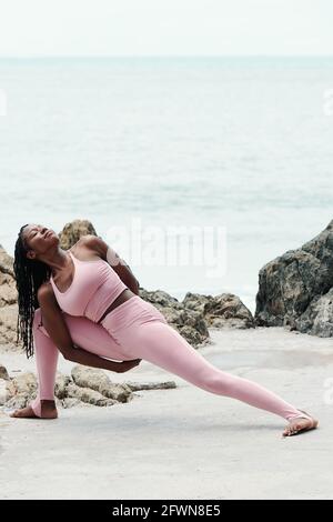 Pretty fit slim young woman doing Utthita parsvakonasana asana on sandy beach Stock Photo