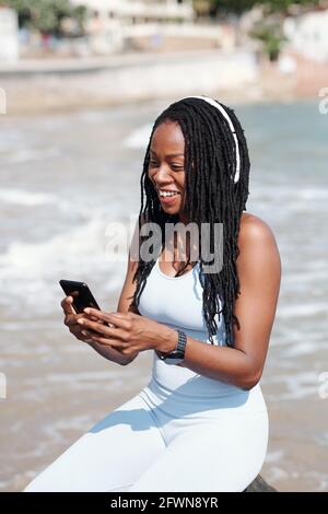 Joyful young woman sitting on beach and video calling her coach or friend Stock Photo