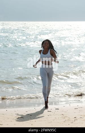 Happy fit beautiful sportswoman in activewear jogging on beach on sunny morning Stock Photo