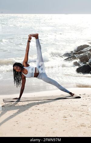 Strong pretty sportswoman doing side plank with leg raise on sea beach in the morning Stock Photo