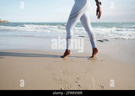 Cropped image of sportswoman in white leggings walking on tiptoes on sandy beach Stock Photo