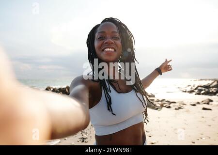 Beautiful smiling young woman with dreadlocks taking selfie on beach after training in the morning Stock Photo