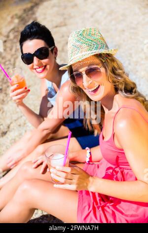 Women drinking cocktails at beach on swimming lake in sand Stock Photo