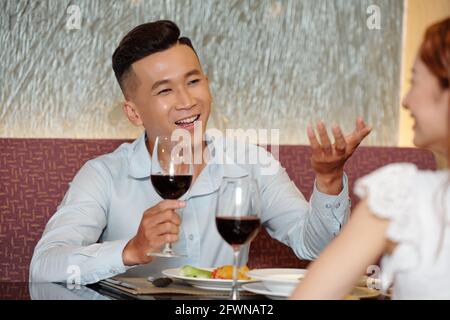 Handsome young man drinking wine and talking with girlfriend at romantic date in restaurant Stock Photo