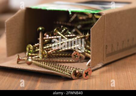 Close-up of open box with long gold new screws on table. Items for repairing or assembling furniture. Advertising, poster for construction store or ma Stock Photo