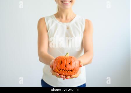 A woman in a white blouse holds a pumpkin for Halloween. Close-up of female hands with a lantern jack on a white background on the eve of All Saints