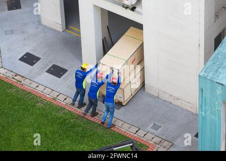 Aerial view of 3 workers pushing the heavy weight crates indoor. Stock Photo