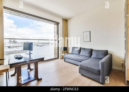 Interior design of workplace with computer on table and gray soft couch in room with view of canal with ships in modern luxury apartment Stock Photo