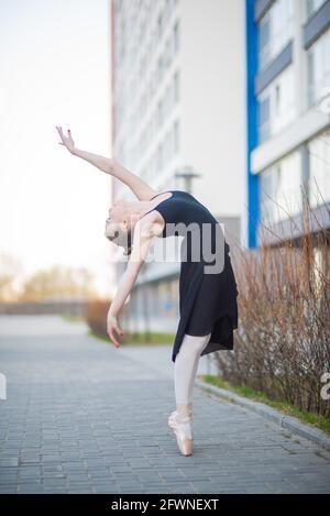Ballerina in a tutu posing in front of a multi-storey residential building. Beautiful woman in black dress and pointe shoes with incredible Stock Photo
