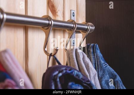 Kid's cloth hanginig on metal hooks on wooden wall. Close-up. Shallow depth of field. Children's jackets in hallway. Country home living.  Stock Photo