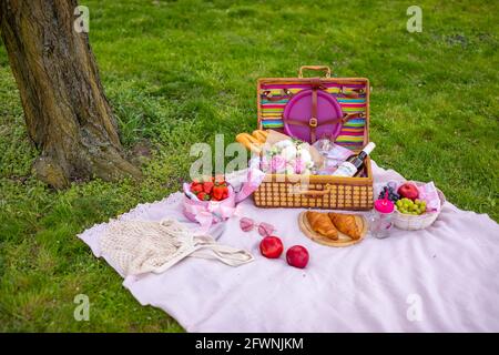Picnic in the park under blooming cherry trees with fruit, wine, bread and croissants Stock Photo