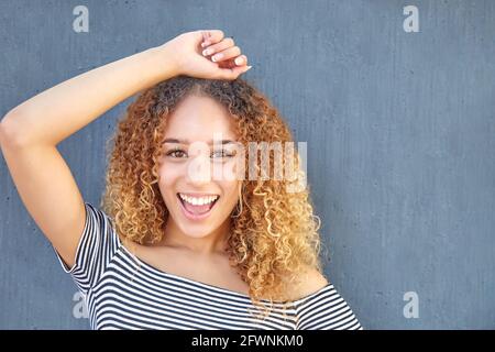 Beautiful curly haired Latina girl smiling on gray background with raised arm. High quality photo Stock Photo