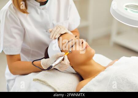 Beautician using electric mesotherapy device to decrease wrinkles on customer's face Stock Photo
