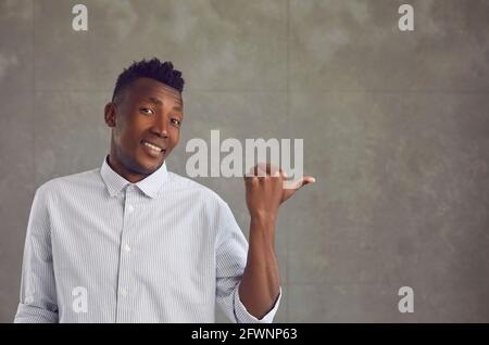 Happy young black man points his thumb at advertising copy space on gray concrete wall Stock Photo