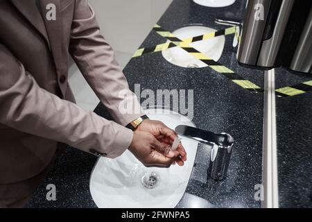 Close up of African-American man washing hands in public restroom with sink taped off for social distancing and covid safety measures, copy space