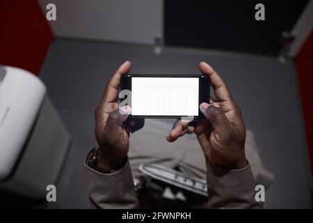 High angle closeup of African-American man using smartphone while sitting on toilet in public restroom, copy space Stock Photo