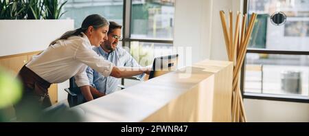 Manager working with colleague and pointing at computer screen. Woman executive showing something to coworker on computer screen in office. Stock Photo