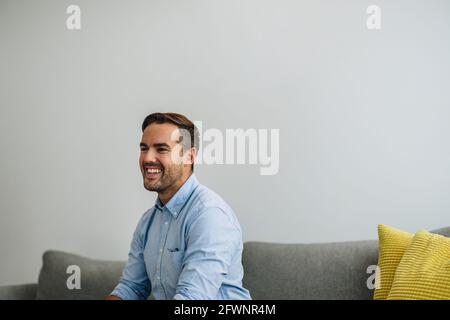 Confident young man sitting on sofa and looking away. Successful businessman smiling in lobby. Stock Photo