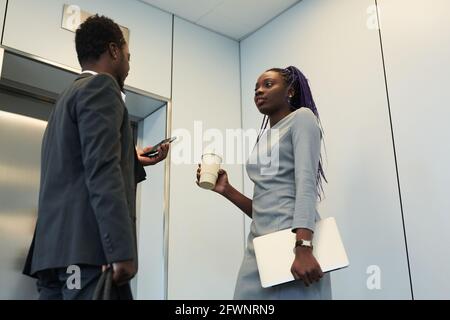 Low angle portrait of two African-American business people waiting for elevator in office building and chatting Stock Photo