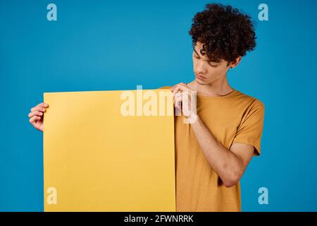 guy with curly hair yellow posters in hands Copy Space blue background studio Stock Photo