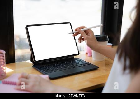 Mockup image of a woman hand using stylus with a black tablet with white blank screen on wooden desk. Stock Photo