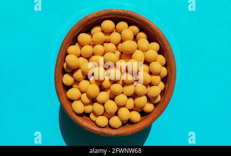 Cheese-coated salted peanuts in a brown bowl on blue background. Fried peanut grains with a coating of savory spices. Top view. Grilled peanuts Stock Photo
