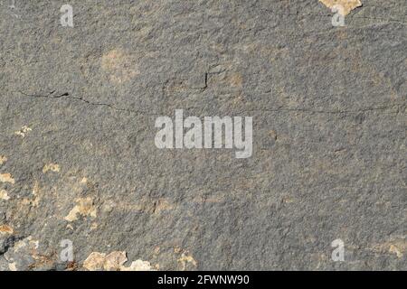 The texture of the surface of gray stone with cracks and light spots of layered rocks. Stock Photo
