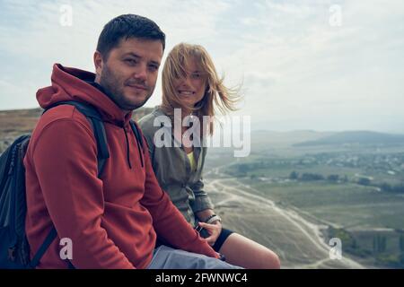 Couple is sitting on the stones, resting, enjoying the view and the fresh air. Hiking concept Stock Photo