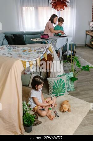Mother teaching her teenage son to iron while her daughter play camping at home Stock Photo